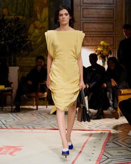 A model on a catwalk wearing a yellow dress with shoulder pads.