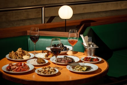 A table lit by lamplight, with three full wine glasses and many plates of food