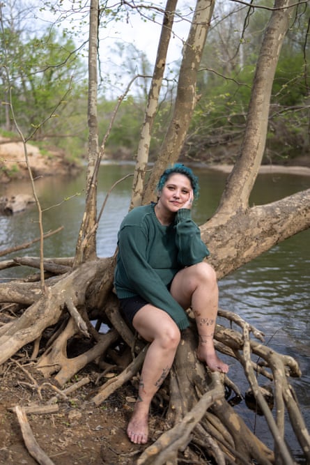 A woman sits for a portrait in tree roots by a creek