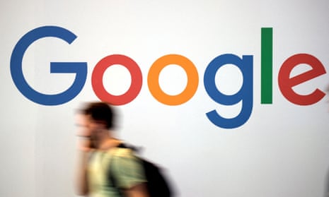 Picture of a person walking past a Google logo on a white wall