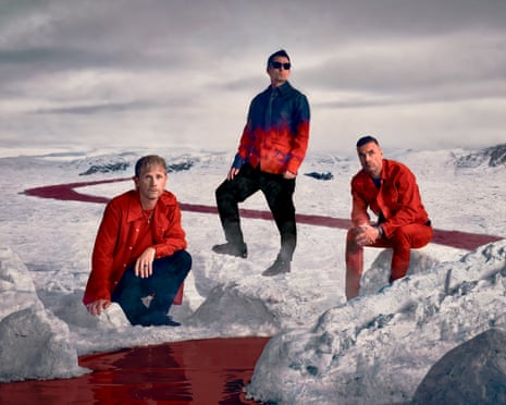 The three members of Muse sitting in a stylised glacial landscape with a blood-red river running through it