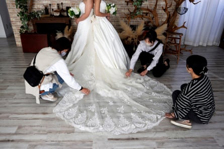 Two women in white wedding dresses with trains pose for a photoshoot in a studio