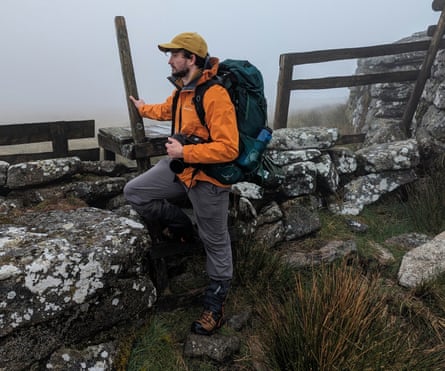 A man by a stone wall with an orange jacket and backpack