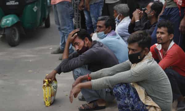 Nirbhay Yadav, 50, in a checked scarf, and his son Lovelesh, left, wait with other migrant labourers in Delhi in hope of a day’s work.