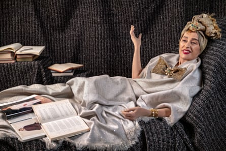 A woman reclines on a sofa dressed in opulent pearls and jewels, with books and magazines lying open at her feet