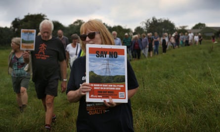 Campaigners walking through a field with posters reading ‘say no’ to electricity pylons
