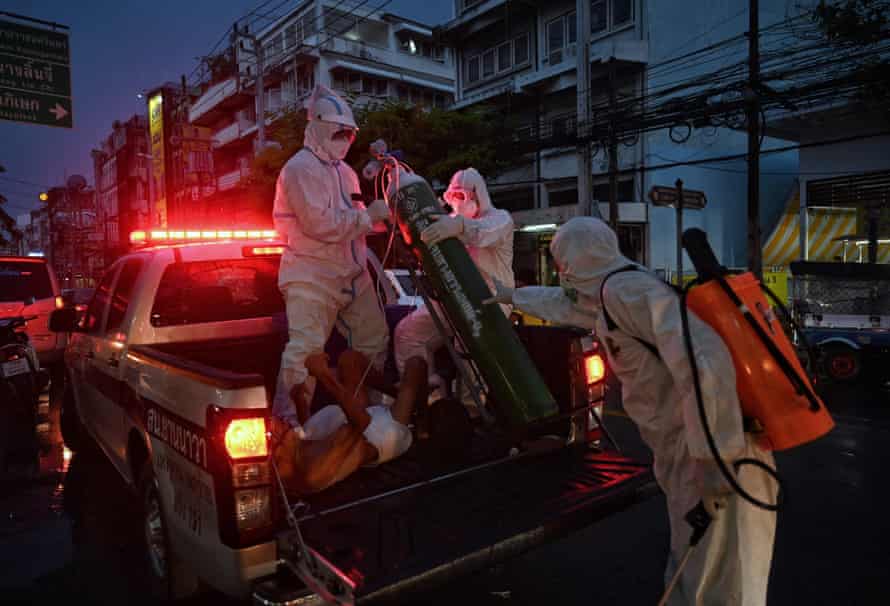 Medics haul an oxygen tank onto the back of a police car for elderly Covid-19 coronavirus patient Worapoj Salee as he is taken away for additional medical care in the Charoen Krung neighbourhood in Bangkok, 30 July.