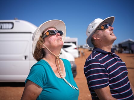 Two people wearing hats and eclipse glasses watch the eclipse