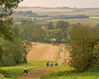 People walking along a path through fields with trees and rolling hills