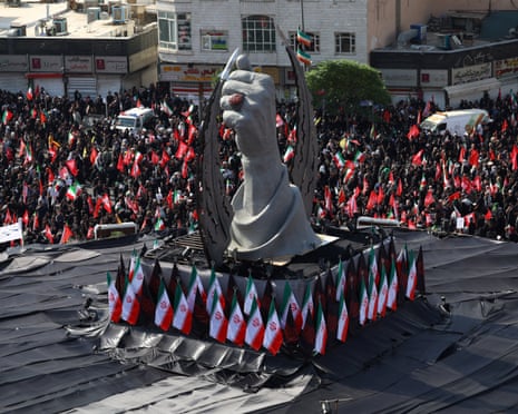 A statue of a fist is in the centre of mourners in black holding flags during national mourning for the former supreme leader of Iran.