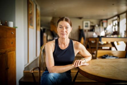 Chef Rachel Marsh sits at a wooden table in a kitchen, her dark red hair tied back in a ponytail, wearing a dark vest and blue jeans