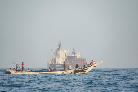People on a small boat with a large freighted container ship in the distance
