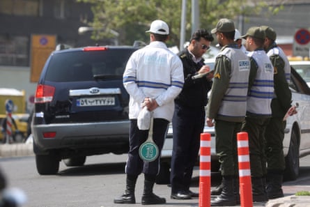 Iranian police officers stand by a traffic barrier preparing to stop cars.