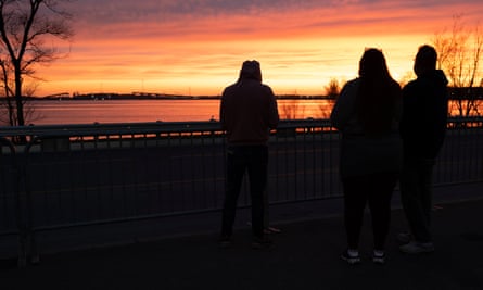 A beautiful pink and yellow sunset across the top half of the frame, with three people in silhouette on the right.