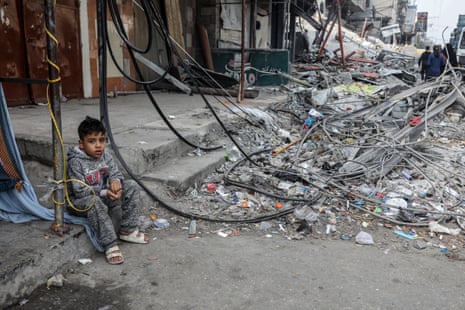 A displaced Palestinian child is seen sitting next to debris on a pavement in Rafah.