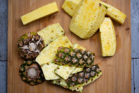 Pineapple slices and pineapple skins on a wooden cutting board.