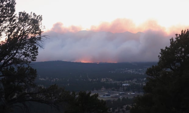 An overall view of Flagstaff, Arizona, with mountains in the distance shrouded by a large plume of smoke with fire glowing orange at its base.