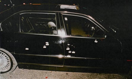Night-time photo of right side of black sedan with bullet holes on both doors and passenger window.