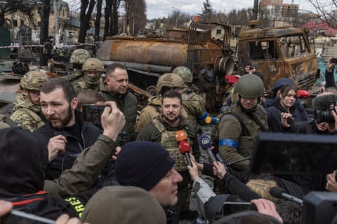 Zelenskyy is surrounded by Ukrainian service personnel in front of a burnt-out tanker as he speaks to reporters