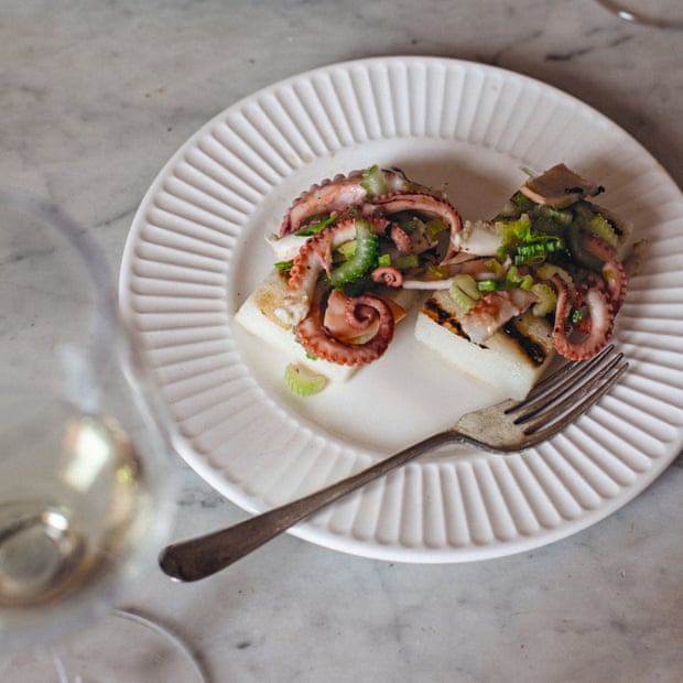 Two portions of baby octopus and celery salad on a white plate next to a glass of white wine