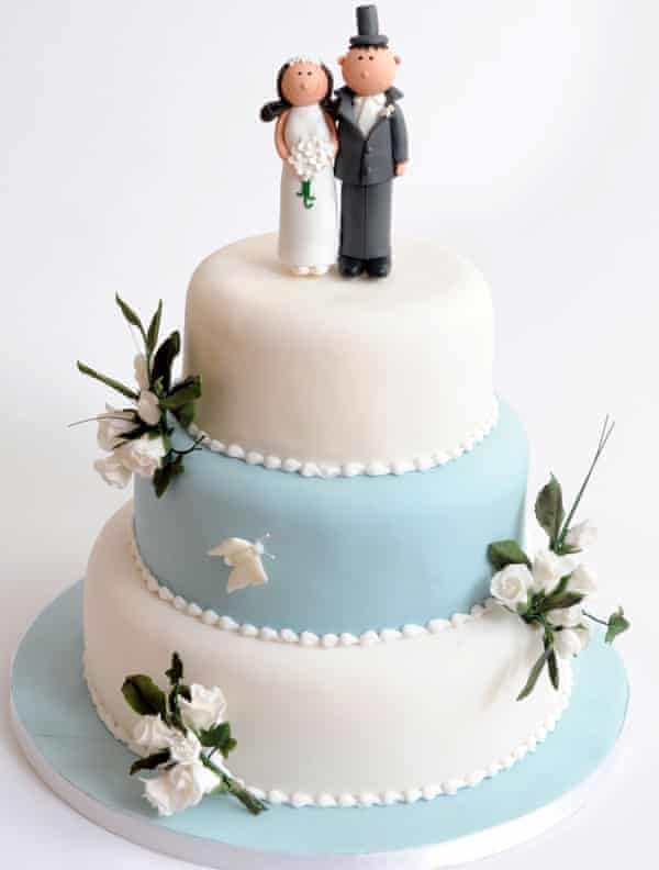 A three-tier wedding cake with decorative flowers and comic bride and groom figure