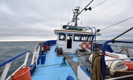 Shot from the bow looking back to a trawler's wheelhouse, blue deck and railings, with a grey sky behind