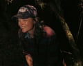 The musician Liz Harris wearing a baseball cap and laughing with her eyes close in shadowy woodland