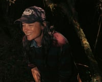 The musician Liz Harris wearing a baseball cap and laughing with her eyes close in shadowy woodland