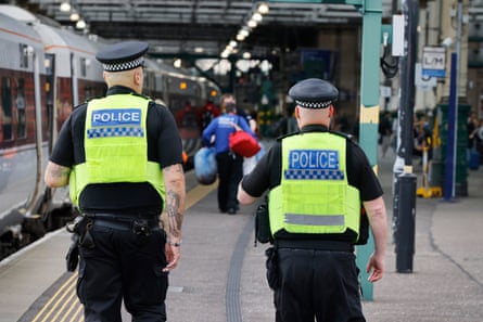 Two transport police in hi-vis jackets walking down a rail platform next to train.