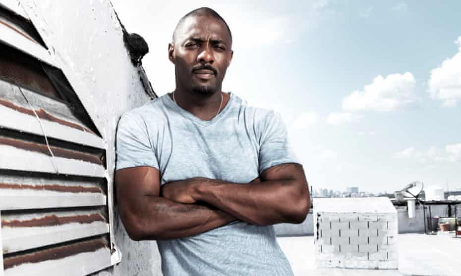 Idris Elba in a pale blue t-shirt on a rooftop