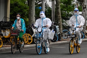 Shanghai, China: Workers wearing personal protective equipment cycle on a street during a Covid-19 coronavirus lockdown in the Jing’an district