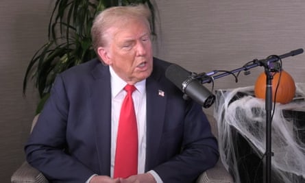Trump, wearing a blue suit and red tie, sits down and speaks into a microphone