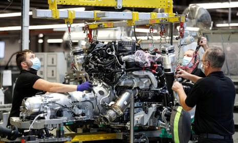 Three men wearing black polo shirts and masks at work on an engine on a production line
