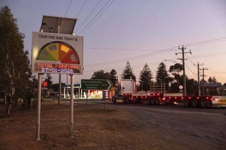 A fire danger sign showing high risk of fires with a total fire ban in place. A sign pointing towards the highway and a parked truck with two empty semi-trailers is in the background