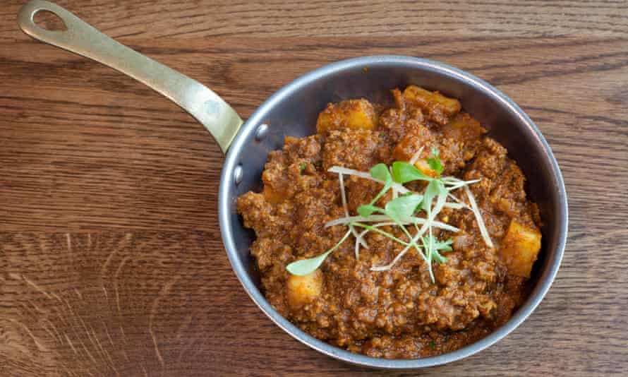 A small frying pan with mutton keema with potatoes and green sprigs on top