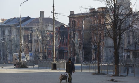 A man walks past damaged buildings in Mariupol