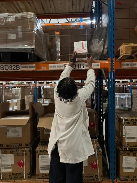 A pharmacist reaches up for a box of lenacapavir on a high shelf in a storage area