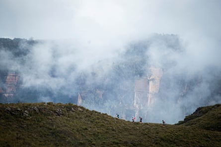 Runners make their way along a ridge, with a cloud-covered mountain looming behind them