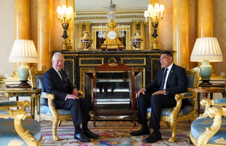 two men in suits speak in a gilded room