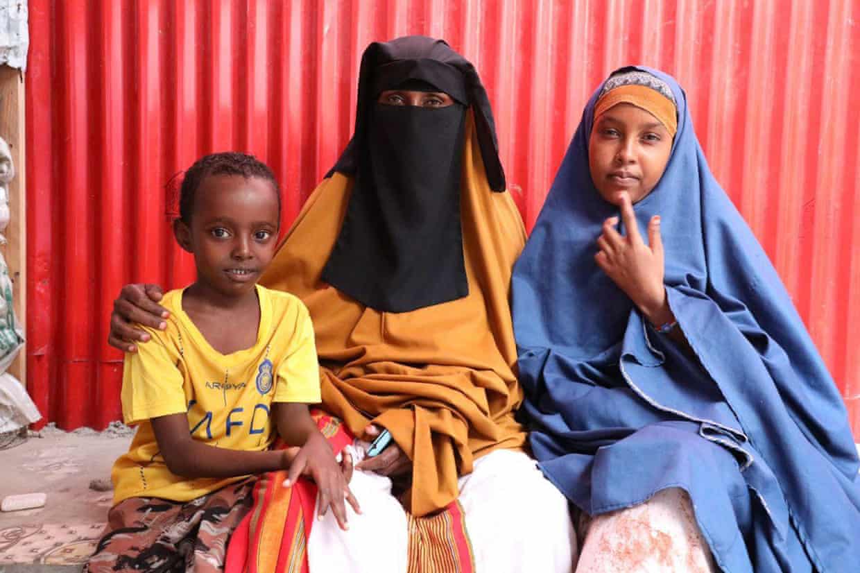 A woman in full veil sits between a young boy and a girl