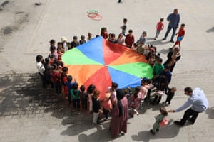 Palestinian children in Gaza City stand in a circle holding a coloured piece of cloth as part of an event to help children process the horrors of war.