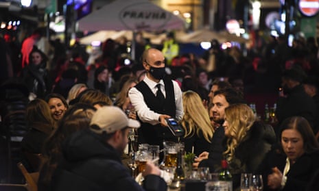 A waiter wears a face mask as people eat and drink outside restaurants in Soho, London