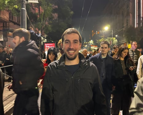 Nemanja smiles amid a crowded, lit street at night, celebrating election results