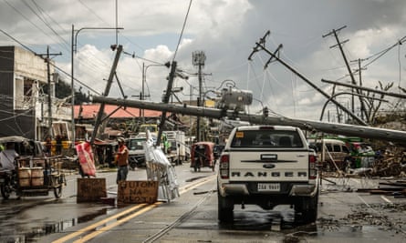 Fallen power poles block a street while a sign asking for food, left, is displayed at the roadside in Surigao City