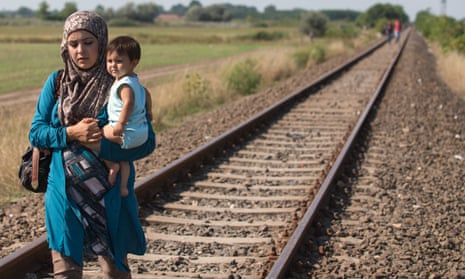 A woman who has just crossed the border from Serbia into Hungary carries her child along a railway line that links the two countries