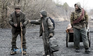 Robert Duvall standing leaning on a long stick on a gravel path