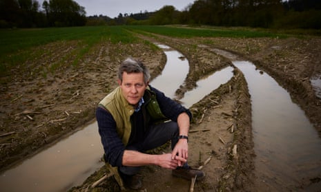 Shropshire farmer Ed Tate kneeling by vehicle tracks filled with water.