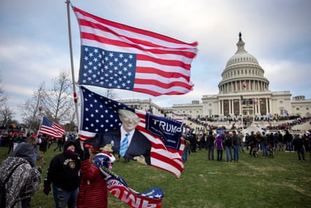 A man with a Trump flag and an upside-down US flag in from of the US Capitol