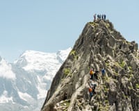 Climbers ascending and at the top of a craggy peak with snowy mountains in the background