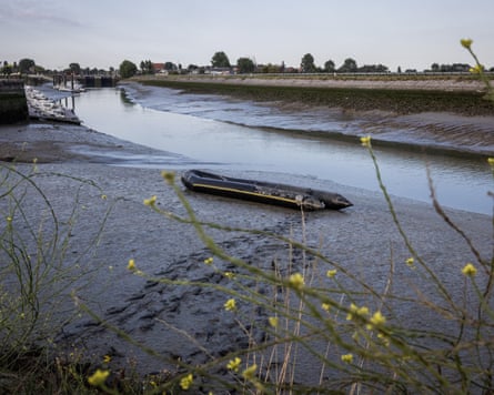 Footprints lead from an inflatable boat in mud next to a canal